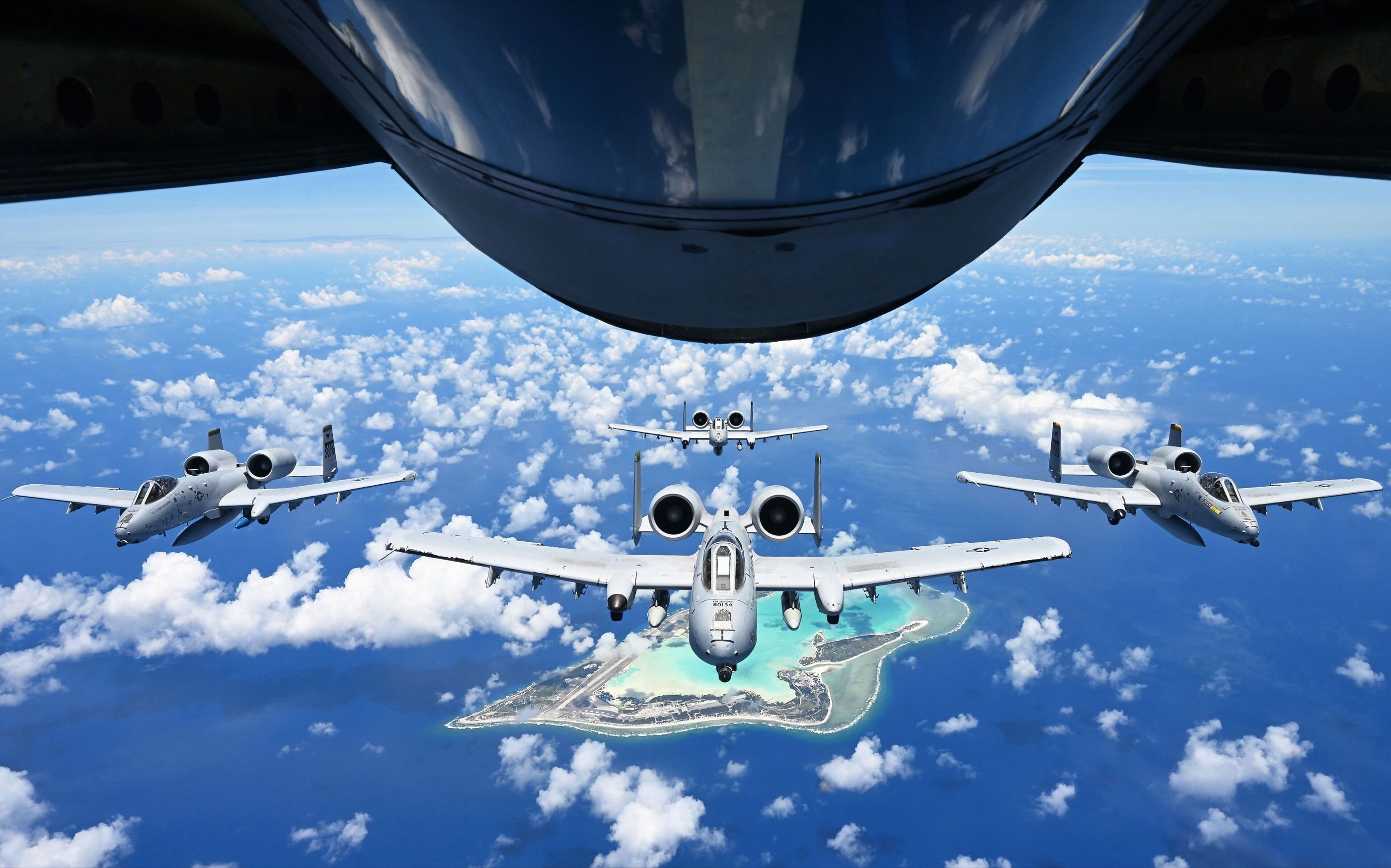 Four A-10s fly in formation behind a tanker's refueling boom over Wake Island