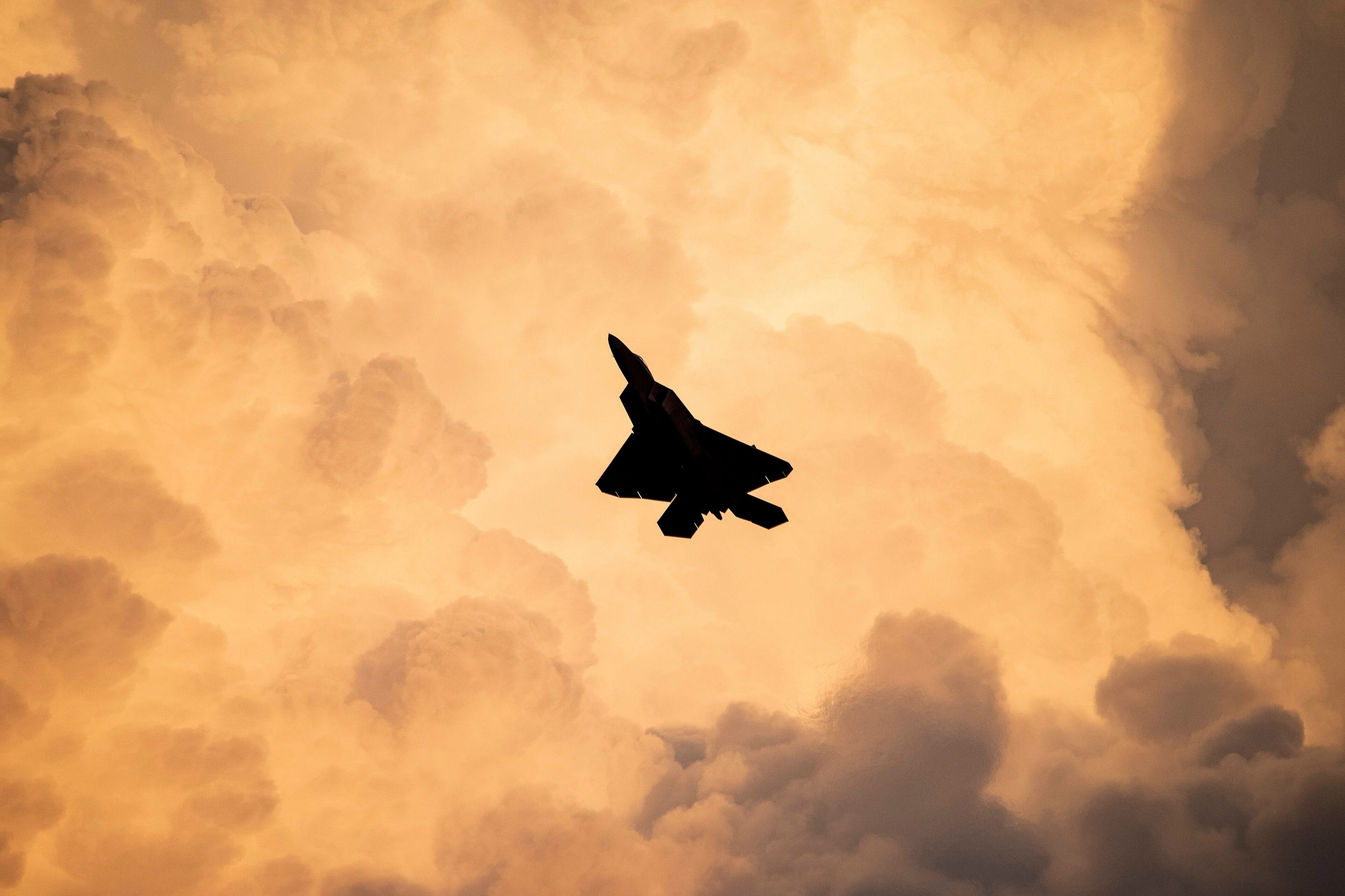 An F-22 Raptor silhouetted against towering storm clouds at twilight